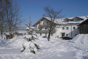 A snow-covered building with a balcony, surrounded by trees and a car parked in front.