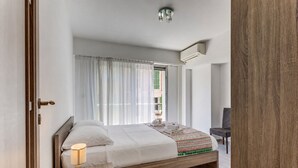 A bedroom with a bed, a bedside table with a lamp, a chair, and a window with curtains. - SUEDE  AP4207 by Riviera Holiday Homes (Niza)