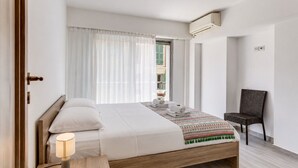 A modern hotel room with a wooden bed, a bedside lamp, a chair, and a view of the outside. - SUEDE  AP4207 by Riviera Holiday Homes (Niza)