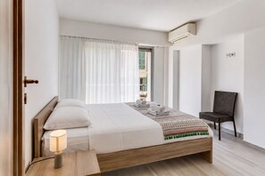 A modern hotel room with a wooden bed, a bedside lamp, a chair, and a view of the outside. - SUEDE  AP4207 by Riviera Holiday Homes (Niza)