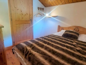 Quarto com cama de madeira, guarda-roupa de madeira e luminária fixada na parede.
