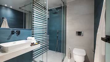 Moderni kylpyhuone, jossa on lasiseinällä varustettu suihku, valkoinen pesuallas ja wc.
