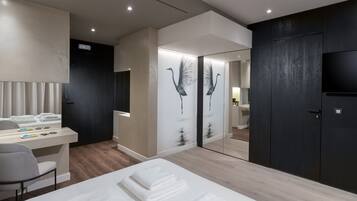 A modern hotel room with a bed, a desk, a chair, a wardrobe, and a television.