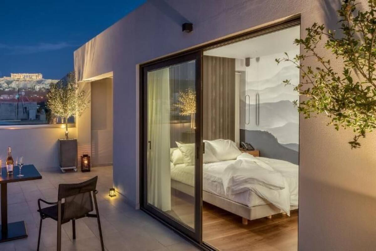 Et moderne hotelværelse med balkon, seng med hvide sengetøj og udsigt til en historisk bygning i baggrunden.