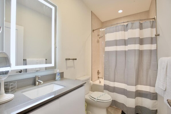 A modern bathroom with a large mirror, a sink, a toilet, and a shower curtain.
