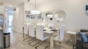 A modern dining area with a white table and chairs, a chandelier, and wall-mounted mirrors. - High luxury NEW 3 bedroom+loft townhouse in Hidden Forest, with private pool! (Clermont)
