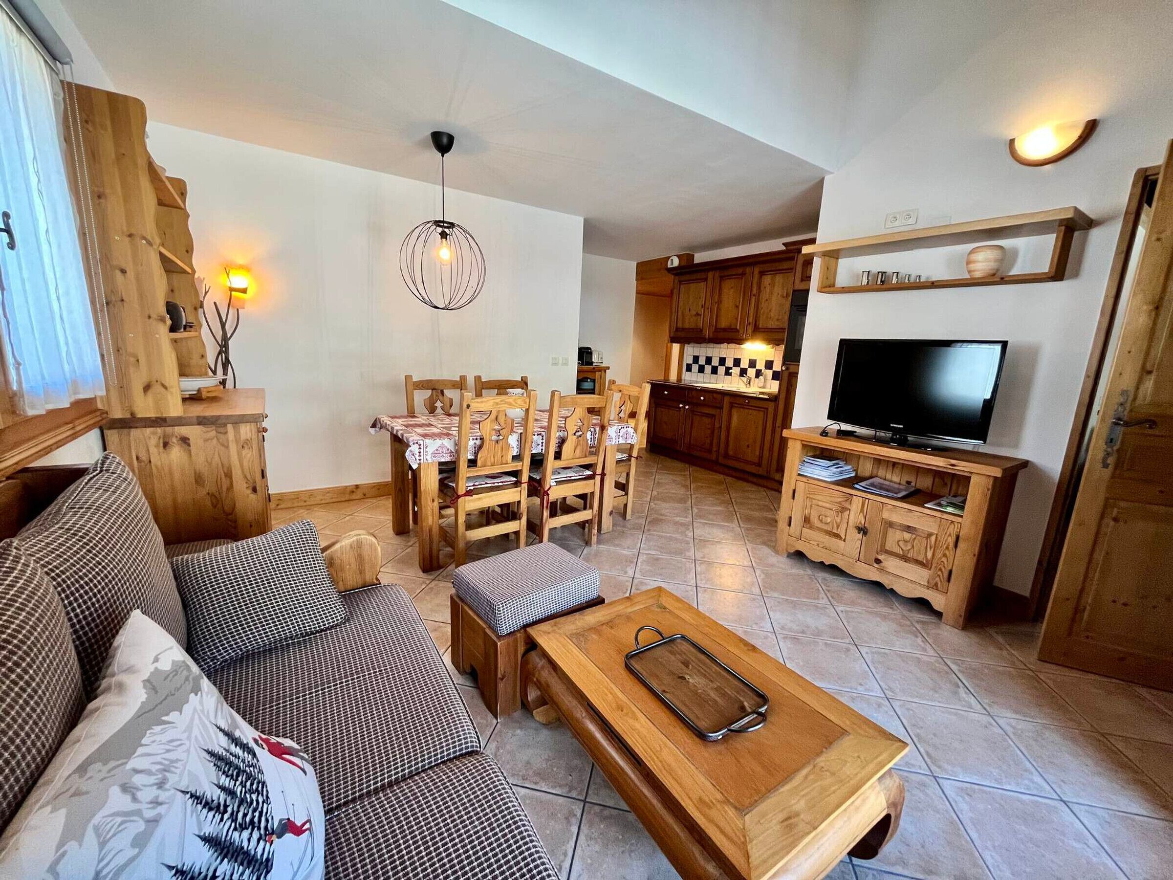 Una sala de estar acogedora con un sofá de madera, una mesa de comedor con sillas, una mesa de centro de madera, un televisor y una zona de cocina con armarios de madera y un estante.