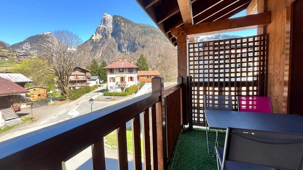 A balcony with a view of a mountain, a table, and chairs.