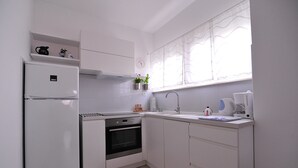 A modern kitchen with white cabinets, a built-in oven, a refrigerator, a sink, and a window with sheer curtains. - A1 - Luxury apt in Center, Just 5min From Beach (Korcula)