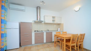 A compact kitchen with a gas stove, a sink, and a built-in oven. There is a dining table with four chairs and a window with curtains. - A2 - apt With 2 Balconies, 5 min Walking to Beach (Podstrana)