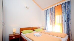 A hotel room with two beds, wooden headboards, a nightstand with a lamp, and a window with patterned curtains. - A7 - apt With 2 Balconies, 5 min Walking to Beach (Podstrana)