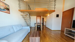 A modern living room with a wooden floor, a light blue sofa, a wooden coffee table, a staircase with a metal railing, and a television on a wooden stand. - A7 - apt With 2 Balconies, 5 min Walking to Beach (Podstrana)