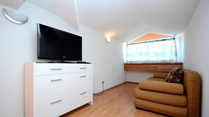 Un salon moderne avec un téléviseur à écran plat posé sur une commode blanche, un canapé marron et une fenêtre avec des rideaux.
