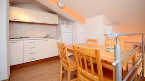 Une cuisine de taille réduite avec des meubles blancs, une table à manger en bois et une cuisinière intégrée.