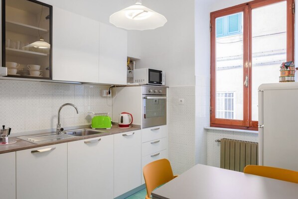 A compact kitchen with a sink, a microwave, a toaster, and a window with shutters.