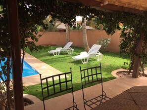 Un jardin avec une piscine, deux chaises longues blanches et une pergola.