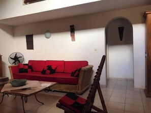 A living room with a red sofa, a wooden chair, a fan, and a small table.