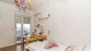 Una camera da letto con un letto, una scrivania, una sedia, un armadio e un balcone con vista sul mare.