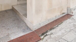 L'ingresso di un edificio con una porta in legno, una finestra con una pianta in vaso e una scalinata in pietra.