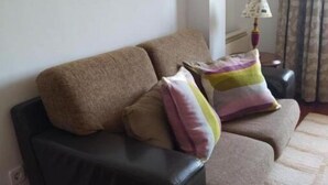 A living room with a black sofa, two cushions, a lamp, and a patterned rug. - Villalomba (Villagarcía de Arosa)