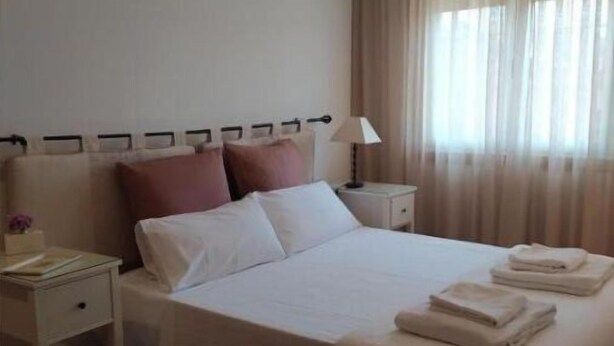 A neatly made bed with white linens and pink pillows, a bedside table with a lamp, and a window with sheer curtains. - Villalomba (Villagarcía de Arosa)