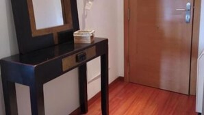 A room with a wooden floor, a dark wooden console table with a mirror, a small white rug, and a closed wooden door. - Villalomba (Villagarcía de Arosa)
