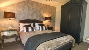 A bedroom with a large bed, two bedside tables with lamps, a dark wardrobe, and patterned wallpaper. - 54 Bridge Street (Brigg)