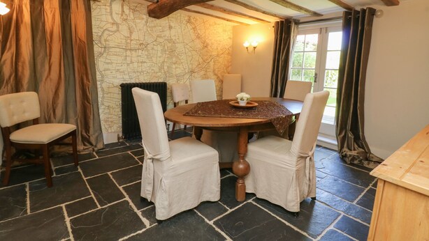 A dining area with a round wooden table, four upholstered chairs, a stone wall, a fireplace, and a window with curtains. - 54 Bridge Street (Brigg)
