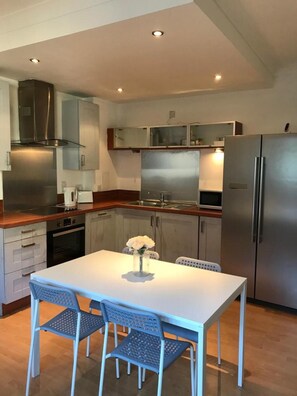 A modern kitchen with stainless steel appliances, a white dining table, and blue chairs. - Apex Variety Gate Apartment (Glasgow)