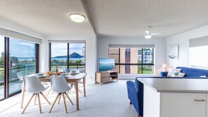 Un soggiorno moderno con zona pranzo, ampie finestre con vista su edifici e una montagna, e una ventola a soffitto.