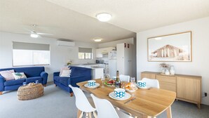 Un soggiorno moderno con un divano blu, un tavolo da pranzo apparecchiato con piatti e bicchieri, e una cucina sullo sfondo.