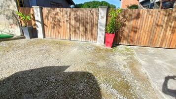 A gravel driveway leading to a wooden gate, with a red planter and a green mat near the gate.