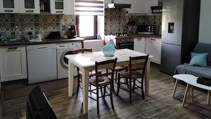 Une cuisine compacte comprenant un coin repas, un lave-linge, un réfrigérateur et une fenêtre avec des stores.