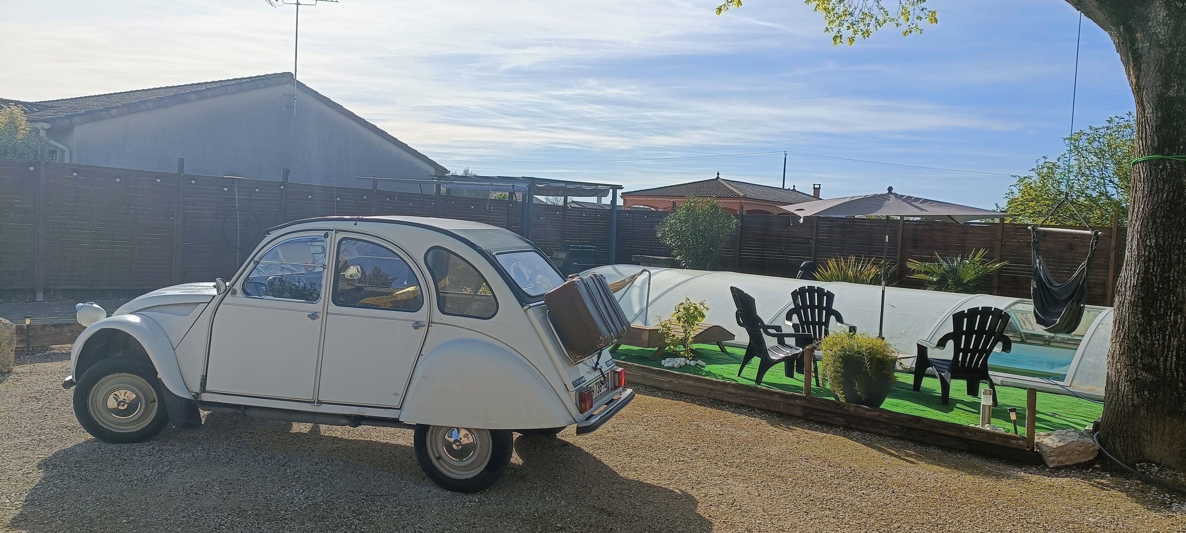 A vintage car parked in a driveway with a garden and outdoor seating area in the background.