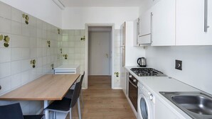 A compact kitchen with a wooden table, chairs, a washing machine, and a stove.