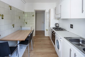 Une cuisine de taille réduite, avec une table en bois, des chaises, un lave-linge et une cuisinière.