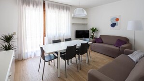 A modern living room with a dining area, a sofa, a TV, and a plant.