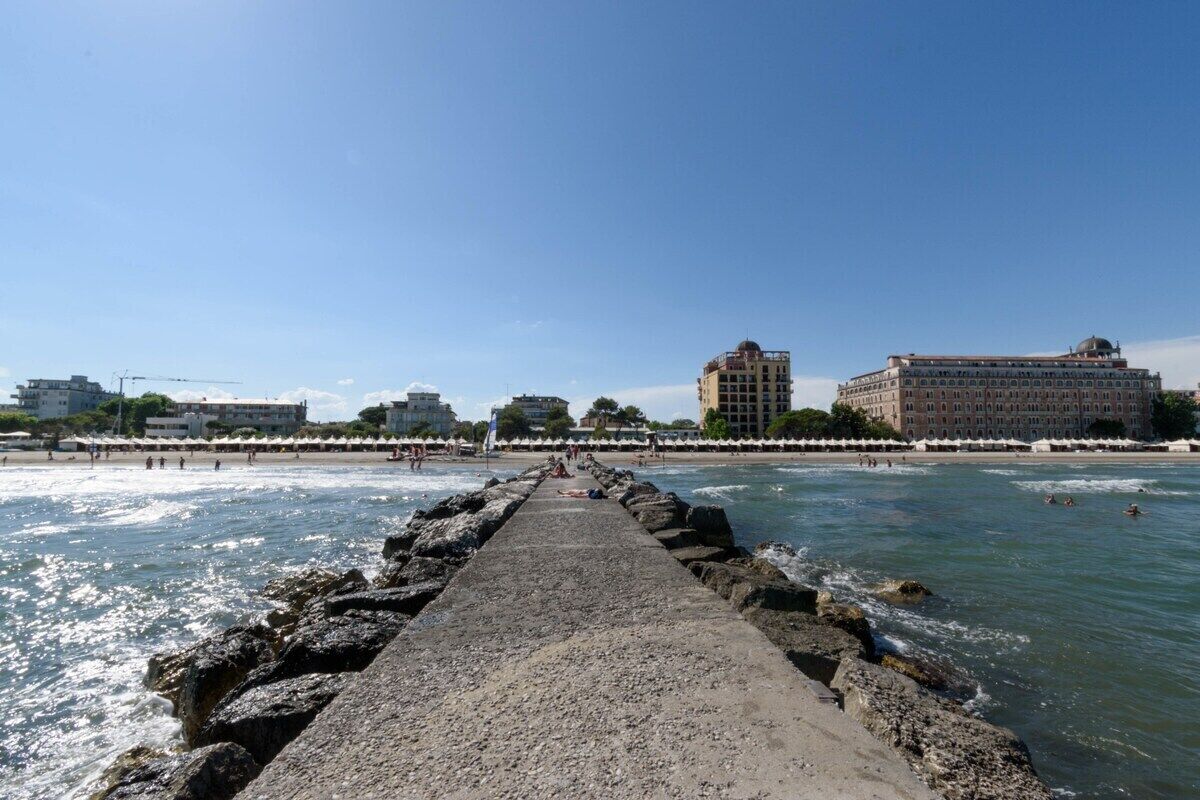 Um píer que dá para uma praia, com edifícios ao fundo.