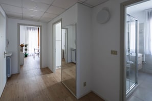 A modern apartment with a wooden floor, a dining area with a chair and table, and a bathroom with a glass shower.