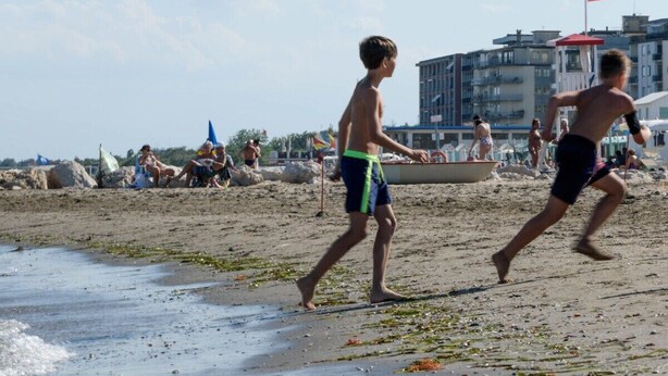 Une plage où l’on voit des gens se promener, une tour de surveillance des sauveteurs et des bâtiments en arrière-plan.