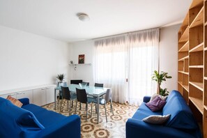 A modern living room with a dining table, blue sofas, and a patterned floor.