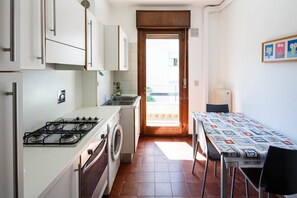 A compact kitchen with a gas stove, washing machine, and a dining area with a table and chairs.
