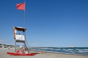 A lifeguard station with a red flag, a lifebuoy, and a beach in the background.