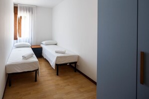 Et lille, rent værelse med to senge, trægulv og et vindue med let gardin.