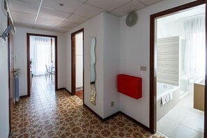 A hallway with patterned flooring, a red cabinet, and a bathroom with a bathtub and shower.