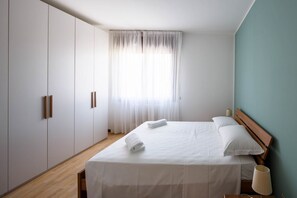A bedroom with a bed, white curtains, a wooden headboard, and a wardrobe.