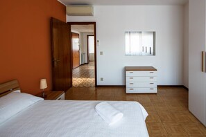 Quarto de hotel com cama, cômoda de madeira, espelho e corredor que leva a outro quarto.
