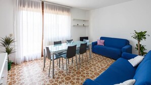 A modern living room with a glass dining table, blue sofa, and patterned floor tiles.