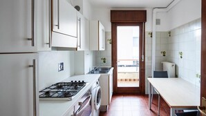 A compact kitchen with white cabinets, a gas stove, a washing machine, and a dining area with a table and chairs.