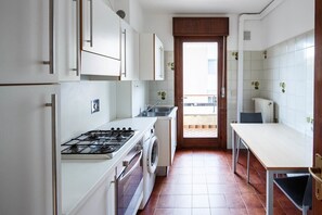 A compact kitchen with white cabinets, a gas stove, a washing machine, and a dining area with a table and chairs.